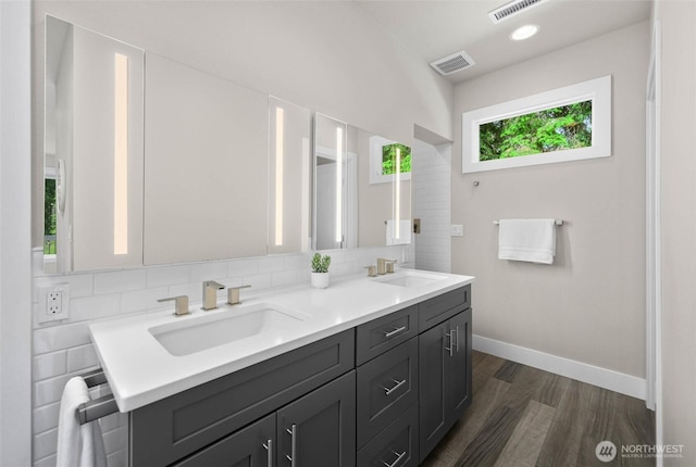 full bath with wood finished floors, baseboards, double vanity, and decorative backsplash
