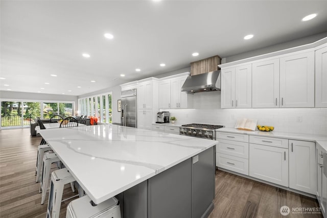 kitchen with wall chimney exhaust hood, built in refrigerator, recessed lighting, tasteful backsplash, and white cabinetry