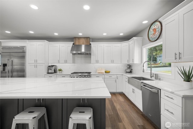 kitchen featuring stainless steel appliances, exhaust hood, a sink, white cabinets, and a breakfast bar area