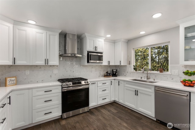 kitchen featuring wall chimney exhaust hood, stainless steel appliances, white cabinets, a sink, and backsplash