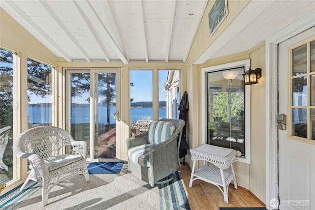 sunroom featuring lofted ceiling with beams, a healthy amount of sunlight, wood finished floors, and a water view