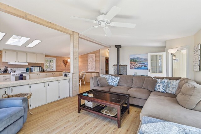 living area with light wood finished floors, wood walls, a wood stove, a ceiling fan, and vaulted ceiling with skylight