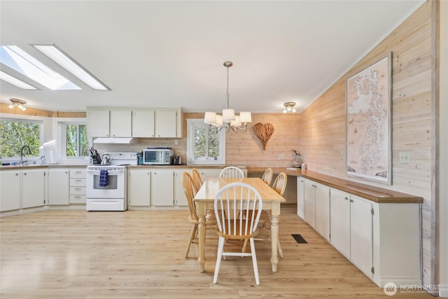 kitchen with wooden walls, light wood-type flooring, electric range, stainless steel microwave, and a notable chandelier