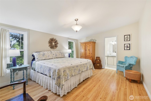 bedroom featuring light wood finished floors, ensuite bath, lofted ceiling, and multiple windows