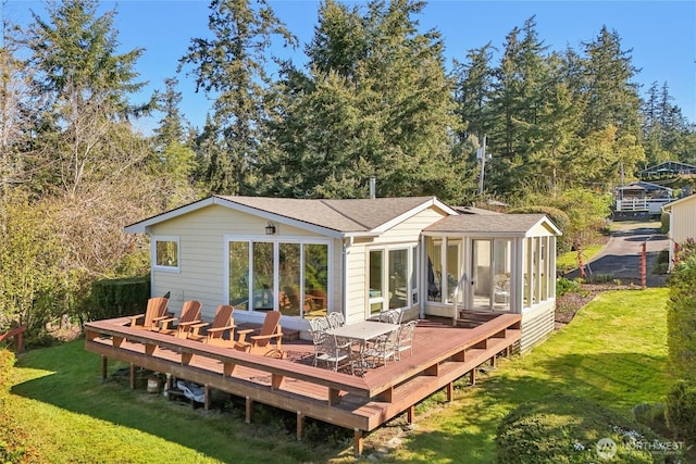 back of property featuring a wooden deck, a sunroom, roof with shingles, and a yard