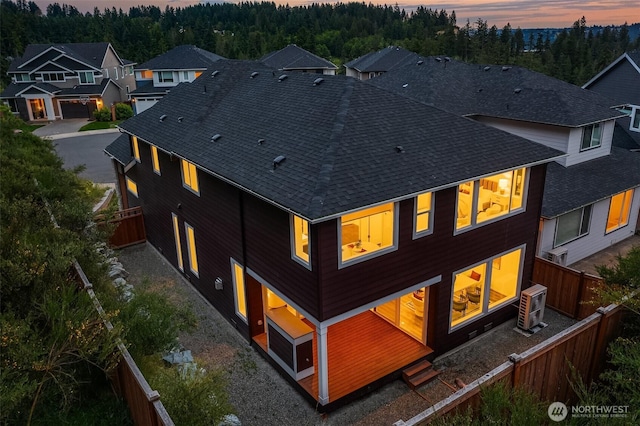 16515 26th St E, Lake Tapps, WA 98391 - back of property at dusk featuring a shingled roof, a fenced backyard, and a wooded view