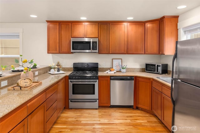 5235 11th Ave NE Unit A, Seattle, WA 98105 - kitchen featuring stainless steel appliances, brown cabinets, recessed lighting, light wood finished floors, and light stone countertops