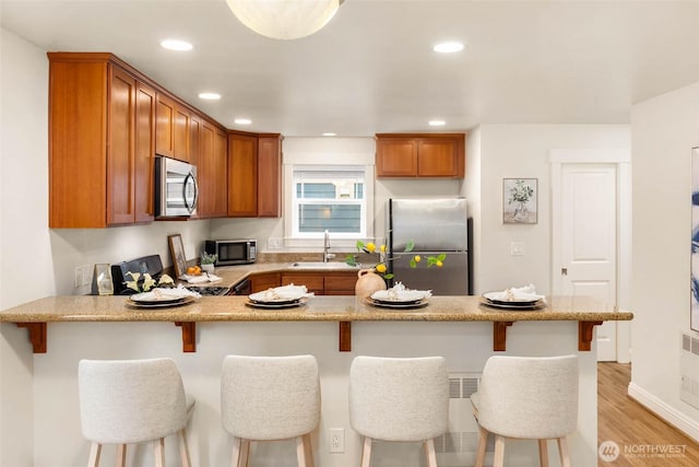 5235 11th Ave NE Unit A, Seattle, WA 98105 - kitchen with stainless steel appliances, a sink, a peninsula, brown cabinets, and light wood-style floors