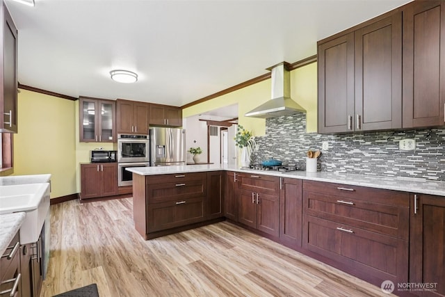 3718 NE Everett St, Camas, WA 98607 - kitchen with appliances with stainless steel finishes, wall chimney exhaust hood, a peninsula, tasteful backsplash, and light wood-style flooring