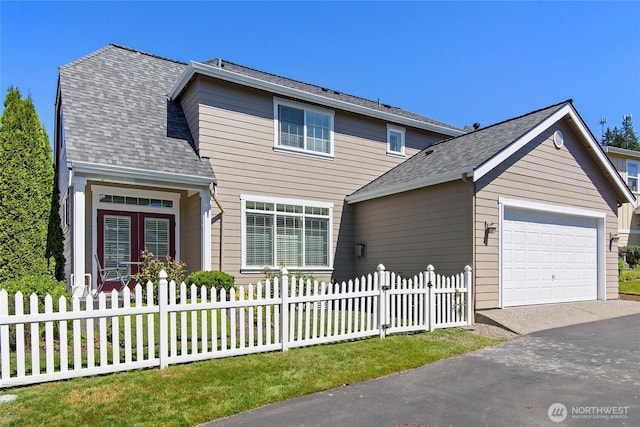 traditional-style house featuring a fenced front yard, an attached garage, and asphalt driveway