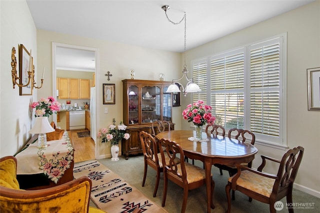dining space featuring a chandelier, baseboards, and light colored carpet