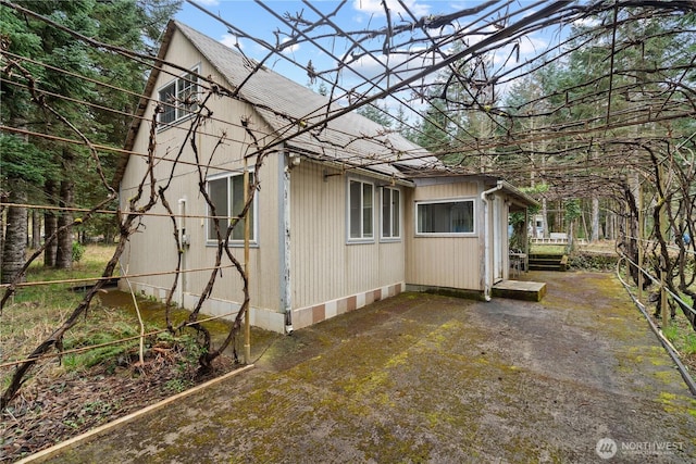 view of side of home with a patio and a shingled roof