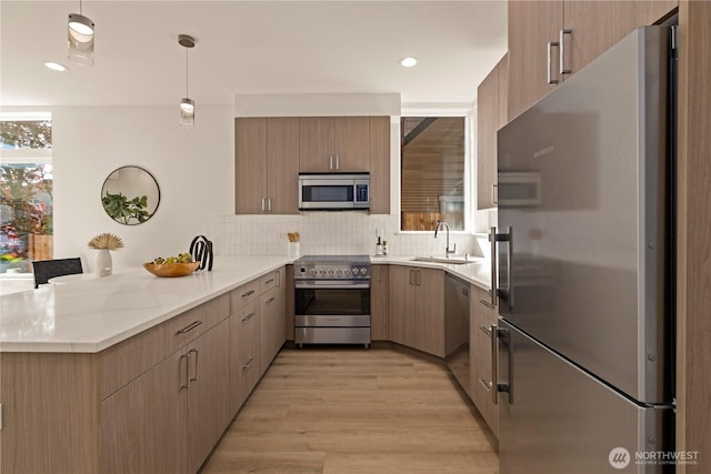 kitchen featuring light wood-style flooring, a sink, a peninsula, stainless steel appliances, and decorative backsplash