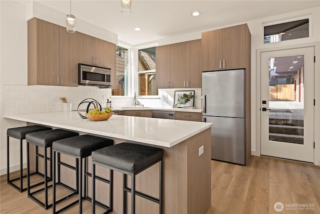 kitchen with light wood-style flooring, a kitchen bar, a peninsula, and stainless steel appliances