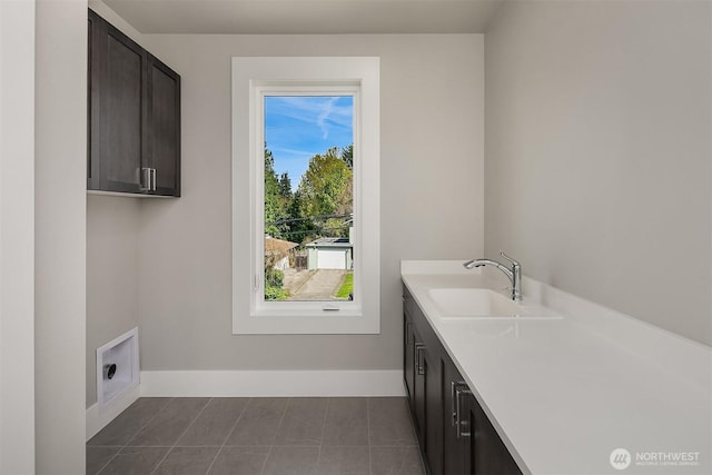 laundry area featuring baseboards, a sink, dark tile patterned floors, and cabinet space