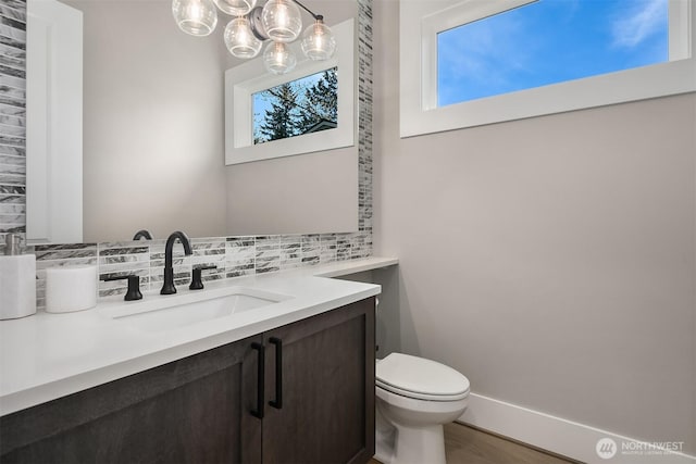 half bathroom with tasteful backsplash, vanity, a chandelier, toilet, and wood finished floors