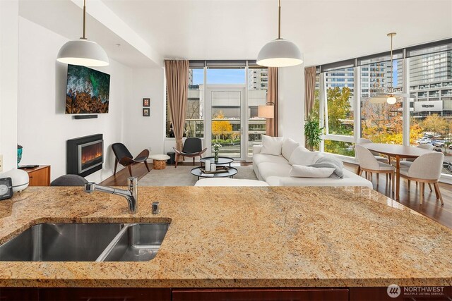 kitchen featuring a sink, open floor plan, a glass covered fireplace, and light stone countertops