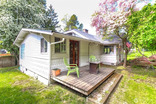 back of property with fence, french doors, a wooden deck, a chimney, and a lawn