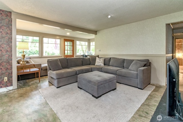 living room with a wainscoted wall, concrete flooring, a textured ceiling, and a wealth of natural light
