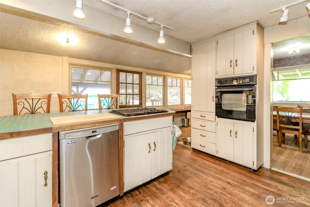 kitchen with cooktop, white cabinets, stainless steel dishwasher, and black oven