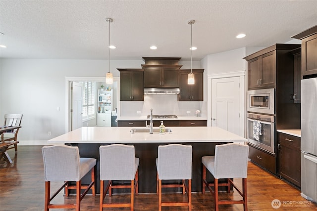 4407 N Ridgefield Woods Dr, Ridgefield, WA 98642 - kitchen featuring appliances with stainless steel finishes, under cabinet range hood, light countertops, a center island with sink, and recessed lighting