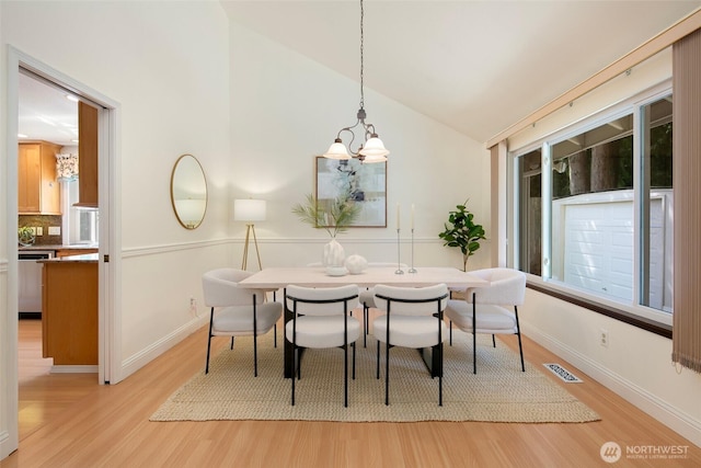 dining space featuring light wood finished floors, lofted ceiling, a chandelier, and baseboards