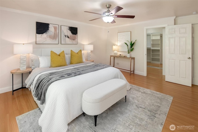 bedroom with baseboards, a walk in closet, ornamental molding, and wood finished floors