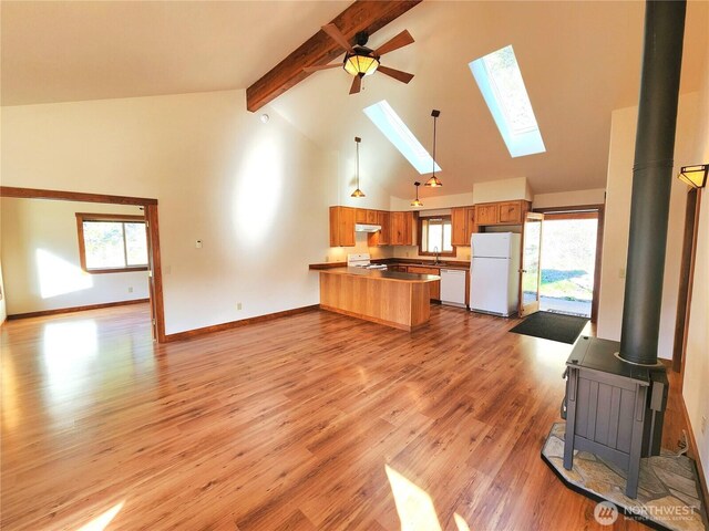 kitchen featuring under cabinet range hood, a wood stove, white appliances, a peninsula, and open floor plan