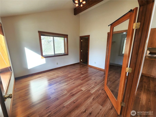 spare room featuring lofted ceiling with beams, baseboards, and wood finished floors