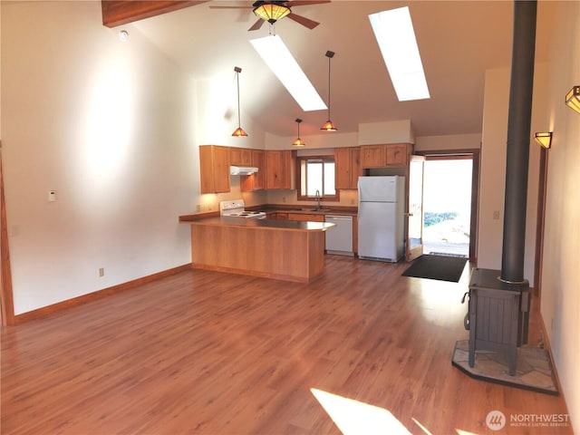 kitchen with a wood stove, a sink, white appliances, a peninsula, and high vaulted ceiling