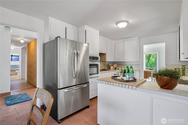 kitchen with stainless steel appliances, light tile patterned floors, a healthy amount of sunlight, and a peninsula