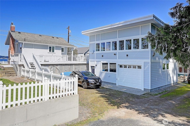 back of house with a chimney, driveway, fence, a garage, and a wooden deck