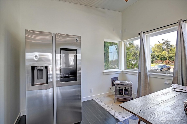 kitchen with a wood stove, stainless steel refrigerator with ice dispenser, and baseboards