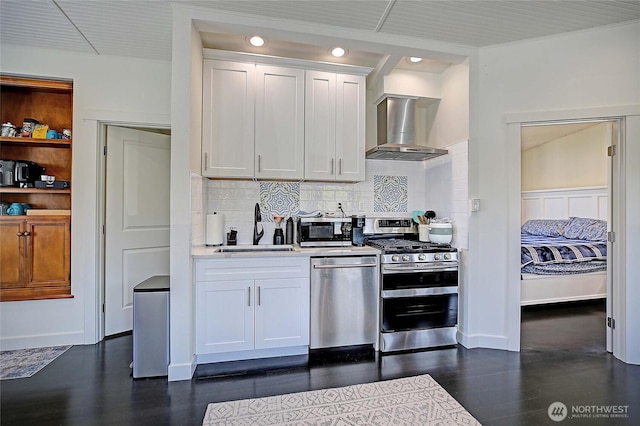 kitchen featuring a sink, white cabinets, backsplash, wall chimney exhaust hood, and appliances with stainless steel finishes