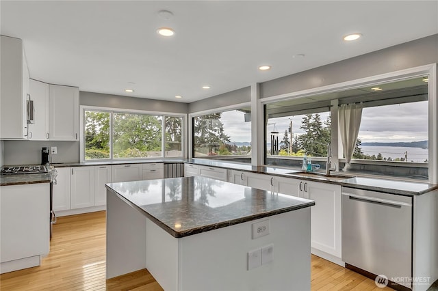 kitchen with appliances with stainless steel finishes, a center island, white cabinetry, a sink, and light wood-style flooring