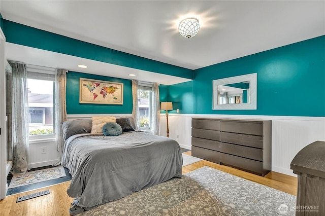 bedroom with a wainscoted wall, wood finished floors, and visible vents
