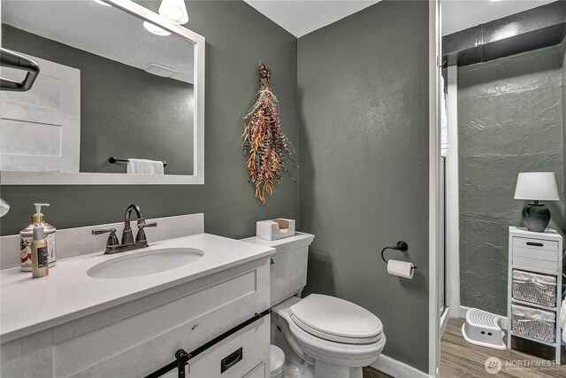 bathroom featuring vanity, wood finished floors, toilet, baseboards, and a shower stall
