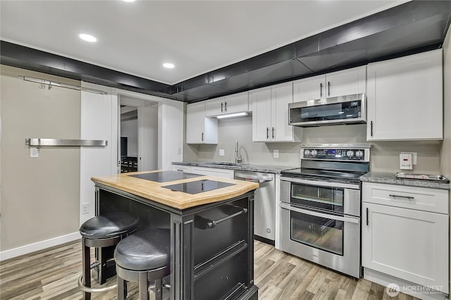 kitchen featuring butcher block countertops, white cabinetry, appliances with stainless steel finishes, and light wood finished floors