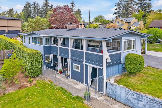 rear view of property featuring a lawn, fence, and a shingled roof
