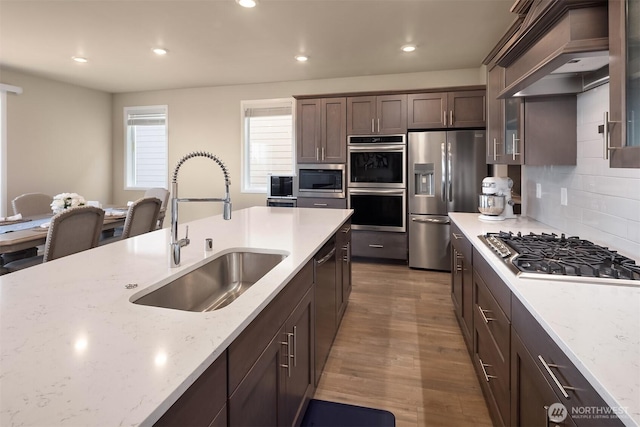 kitchen with a sink, custom exhaust hood, dark brown cabinetry, wood finished floors, and appliances with stainless steel finishes