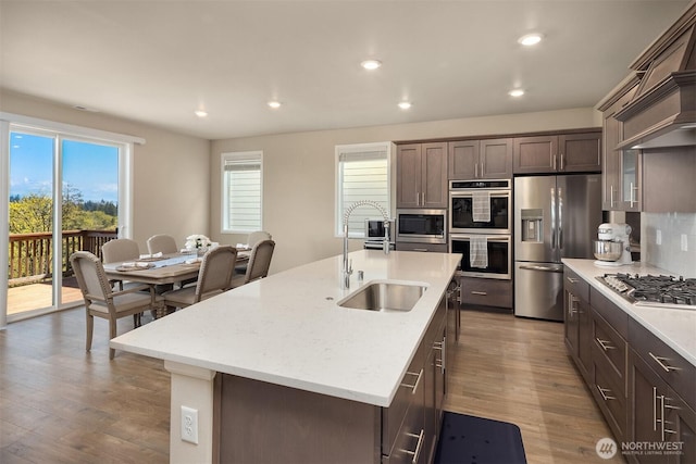 kitchen with a sink, dark brown cabinets, recessed lighting, wood finished floors, and appliances with stainless steel finishes