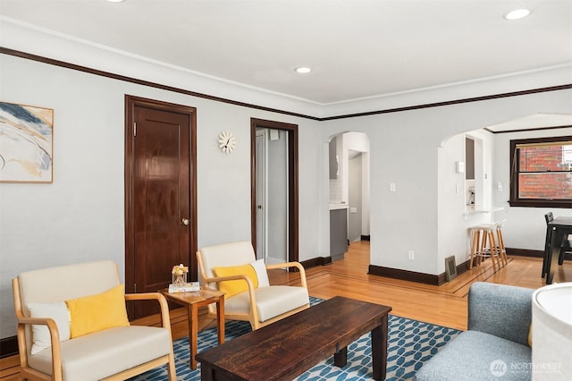living room featuring crown molding, arched walkways, baseboards, recessed lighting, and light wood-style flooring