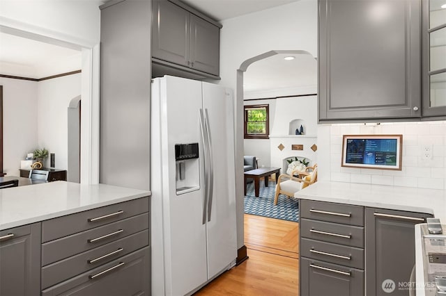 kitchen featuring white refrigerator with ice dispenser, light countertops, arched walkways, gray cabinets, and light wood-style flooring