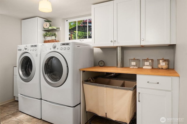 clothes washing area featuring baseboards, washing machine and dryer, and cabinet space