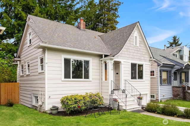 view of front of property featuring roof with shingles, fence, a front yard, and a chimney