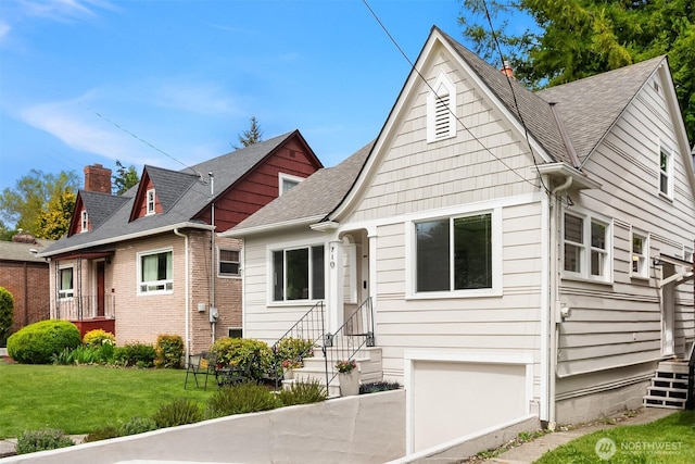 view of front of home featuring roof with shingles, a front yard, entry steps, and a garage