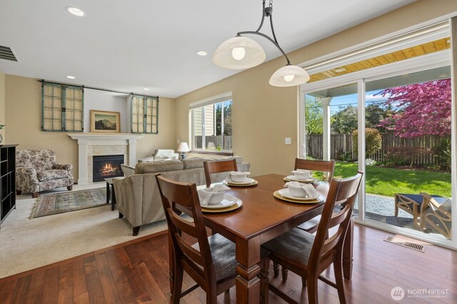 dining space with recessed lighting, a warm lit fireplace, visible vents, and dark wood-type flooring
