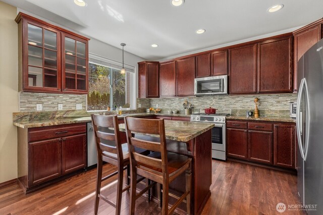 kitchen with decorative light fixtures, appliances with stainless steel finishes, dark stone counters, recessed lighting, and dark wood-type flooring