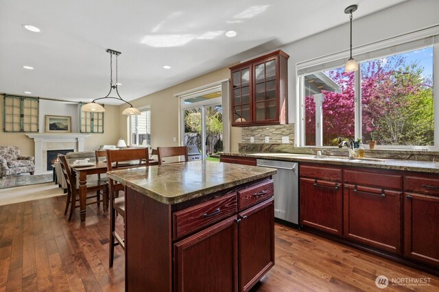 kitchen featuring a lit fireplace, stainless steel dishwasher, dark brown cabinets, a sink, and a breakfast bar