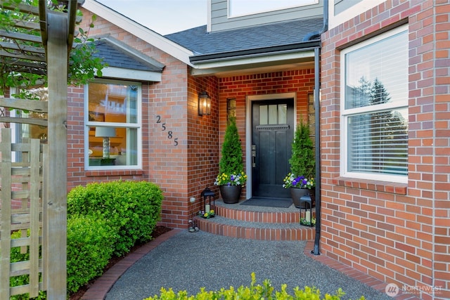 entrance to property featuring brick siding and roof with shingles